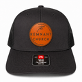A black trucker-style cap with a curved brim, black mesh back, and a circular orange front patch reading 'The REMNANT CHURCH.' A size/brand sticker is visible on the brim.