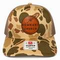 A camouflage trucker hat with brown mesh back panels, featuring a circular brown leather patch on the front that reads 'The REMNANT CHURCH' and a white size patch on the brim.