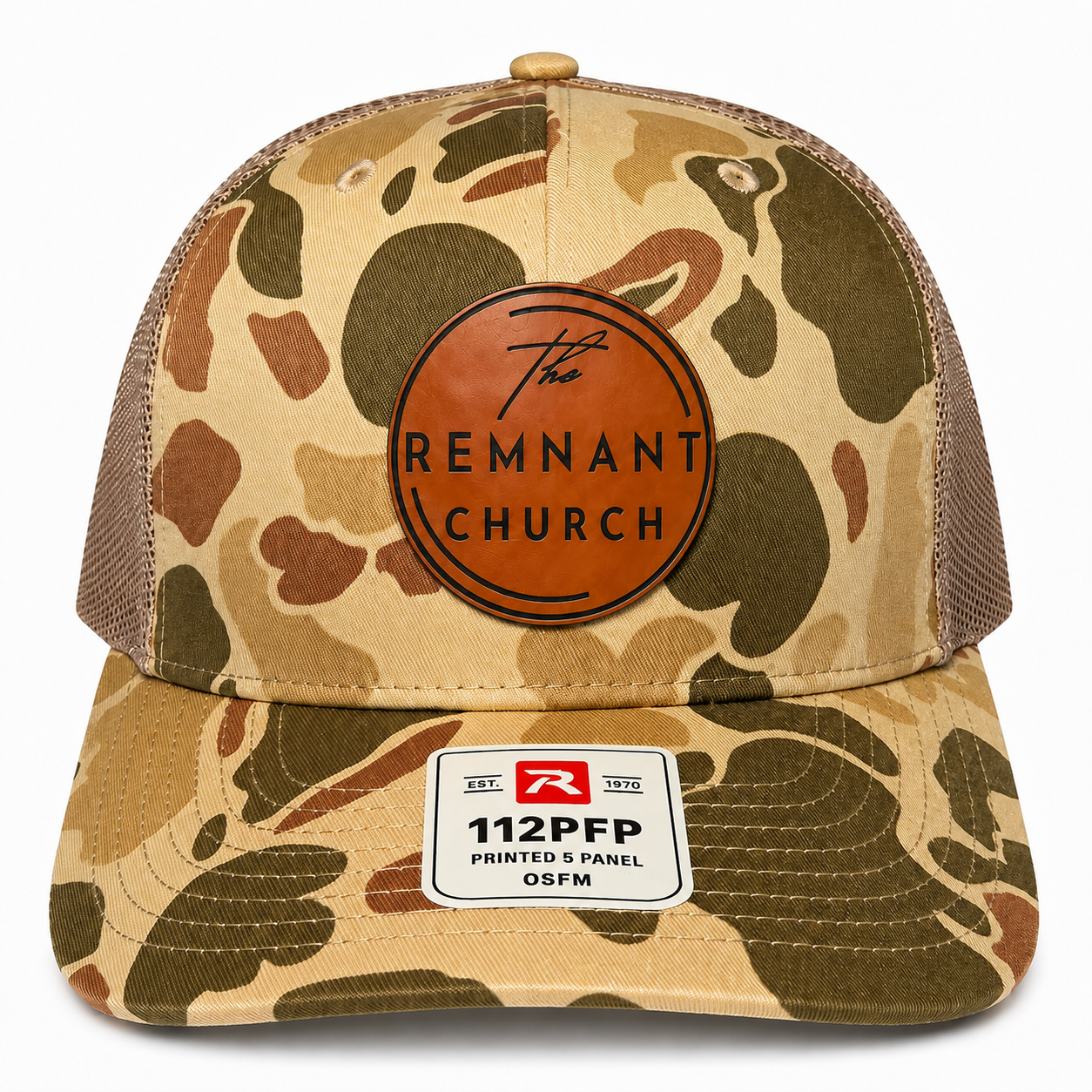 A camouflage trucker hat with brown mesh back panels, featuring a circular brown leather patch on the front that reads 'The REMNANT CHURCH' and a white size patch on the brim.